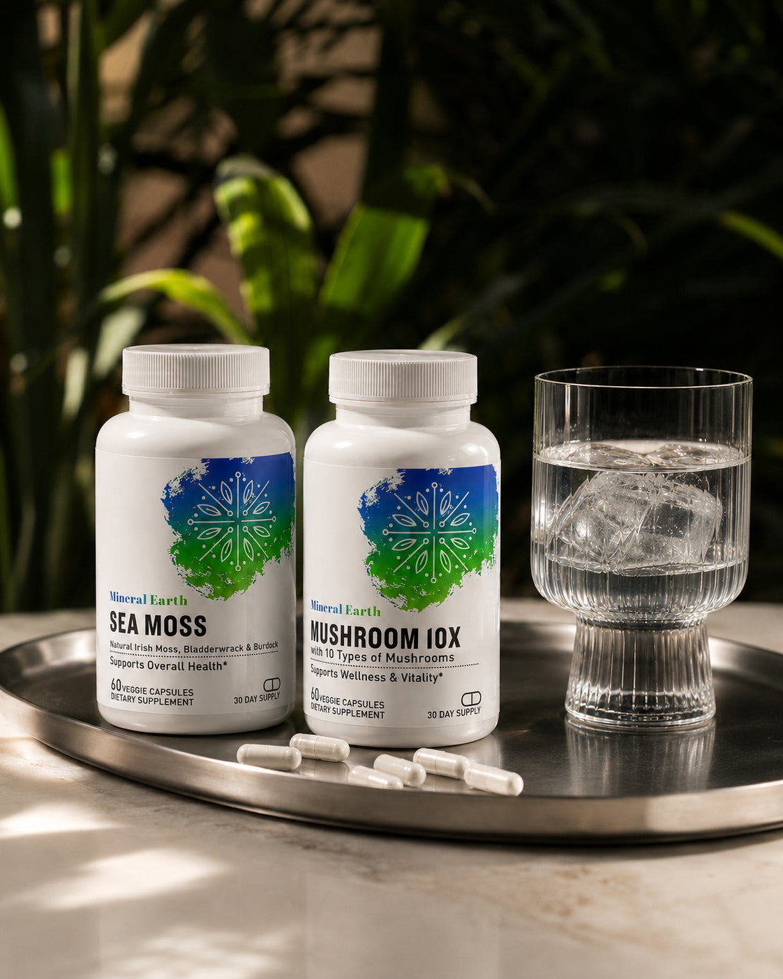 Mineral Earth Sea Moss and Mushroom 10X supplement bottles with capsules and glass of water on silver tray